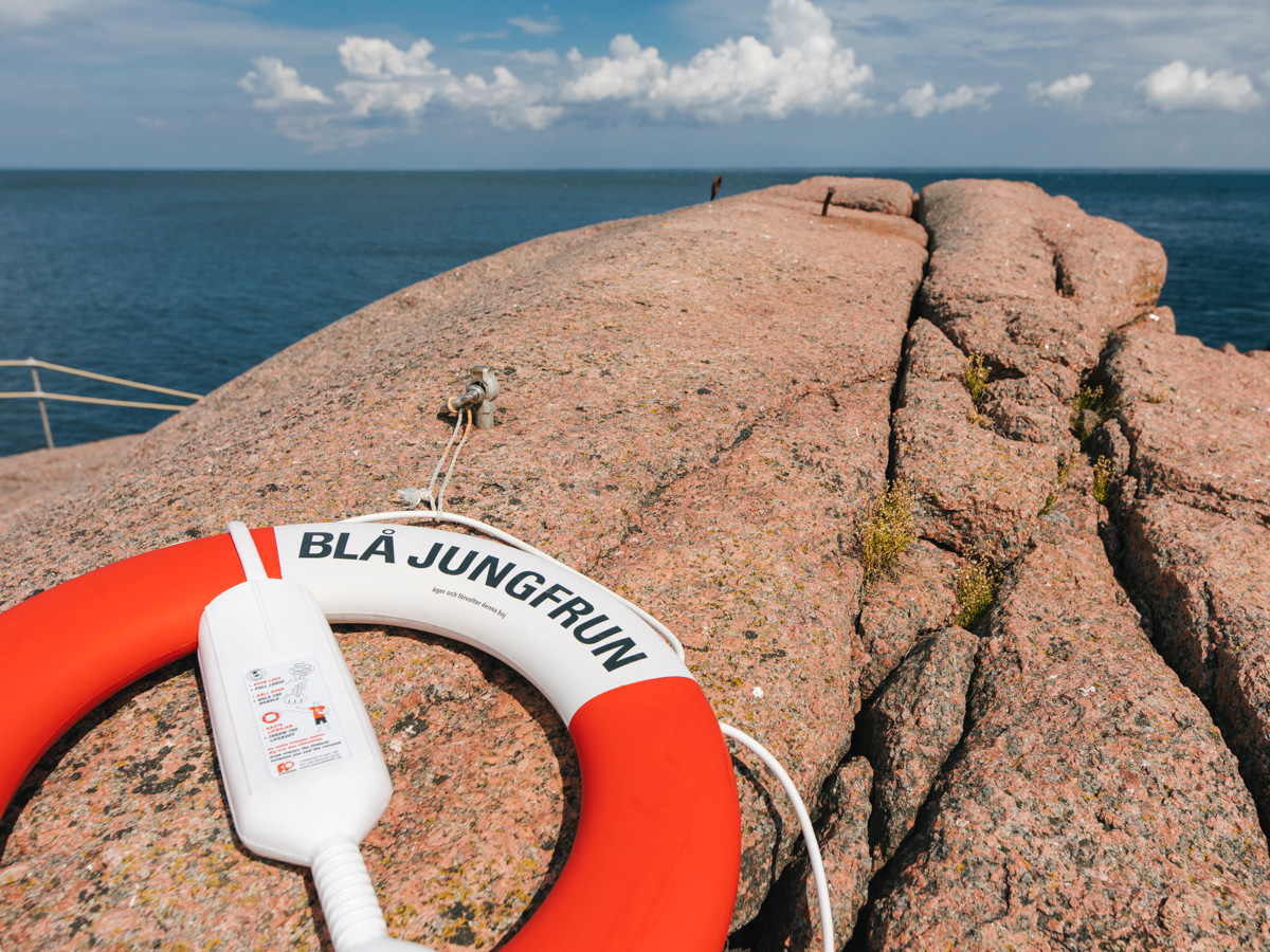 Röd livboj märkt Blå Jungfrun på öns rosa granithällar, med havet bakom